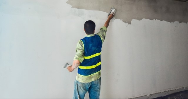Người thợ đang thi công bả tường chuyên nghiệp bằng bay và bàn bả, tạo ra bề mặt láng mịn.